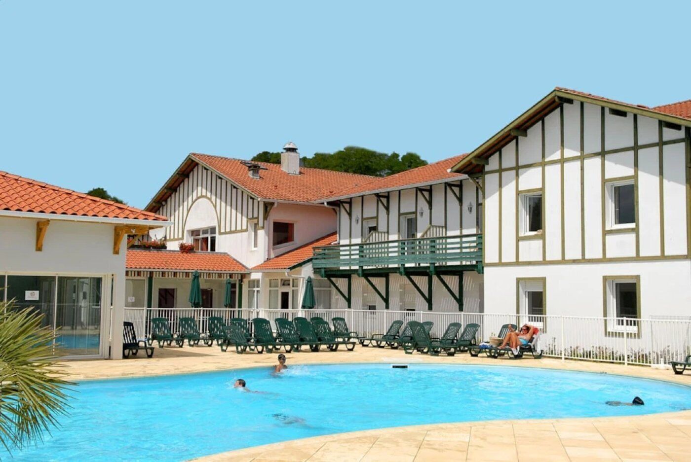 Une piscine avec des chaises longues et un bâtiment doté d’un balcon.