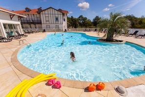 Ein Schwimmbecken mit Liegestühlen und einem Gebäude im Hintergrund.