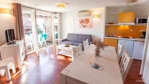Ein modernes Hotelzimmer mit Balkon, einer Couch, einem Esstisch und einer Küchenzeile.
