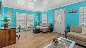 Un salon aux murs de couleur turquoise, avec un bureau en bois, un canapé beige et une table basse en verre.