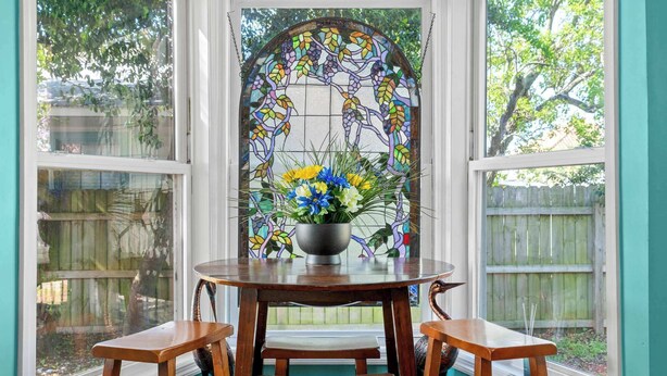Une baie vitrée ornée de vitraux, une table avec des chaises et un arrangement floral.
