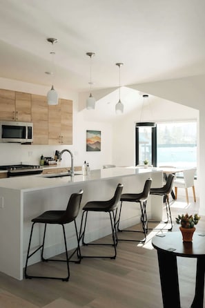 A modern kitchen with a central island, bar stools, a microwave, and pendant lighting.