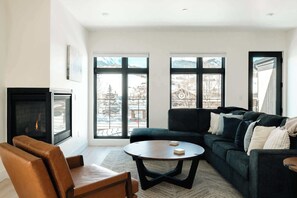 A living room with a fireplace, a sofa, a coffee table, and large windows with a view.