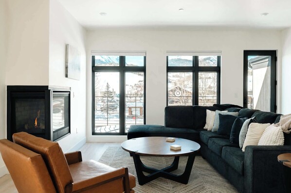 Un salon avec une cheminée, un canapé, une table basse et de grandes fenêtres offrant une vue dégagée.