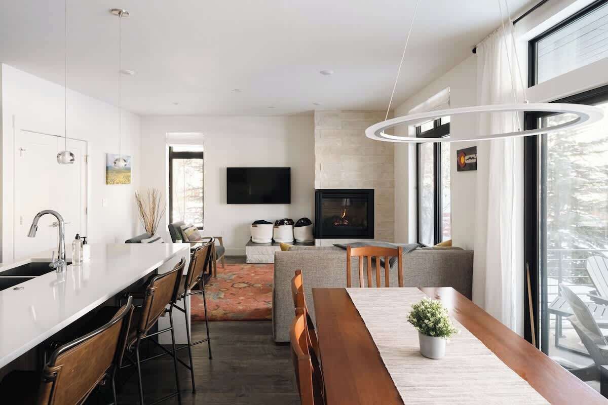 A modern kitchen with a central island, a dining area with a wooden table, and a fireplace.