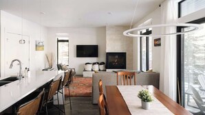 Une cuisine moderne dotée d’un îlot central, d’un coin repas avec une table en bois et d’une cheminée.