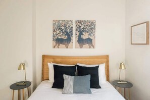 A bed with a wooden headboard, two black pillows, a grey pillow, and two bedside tables with lamps.