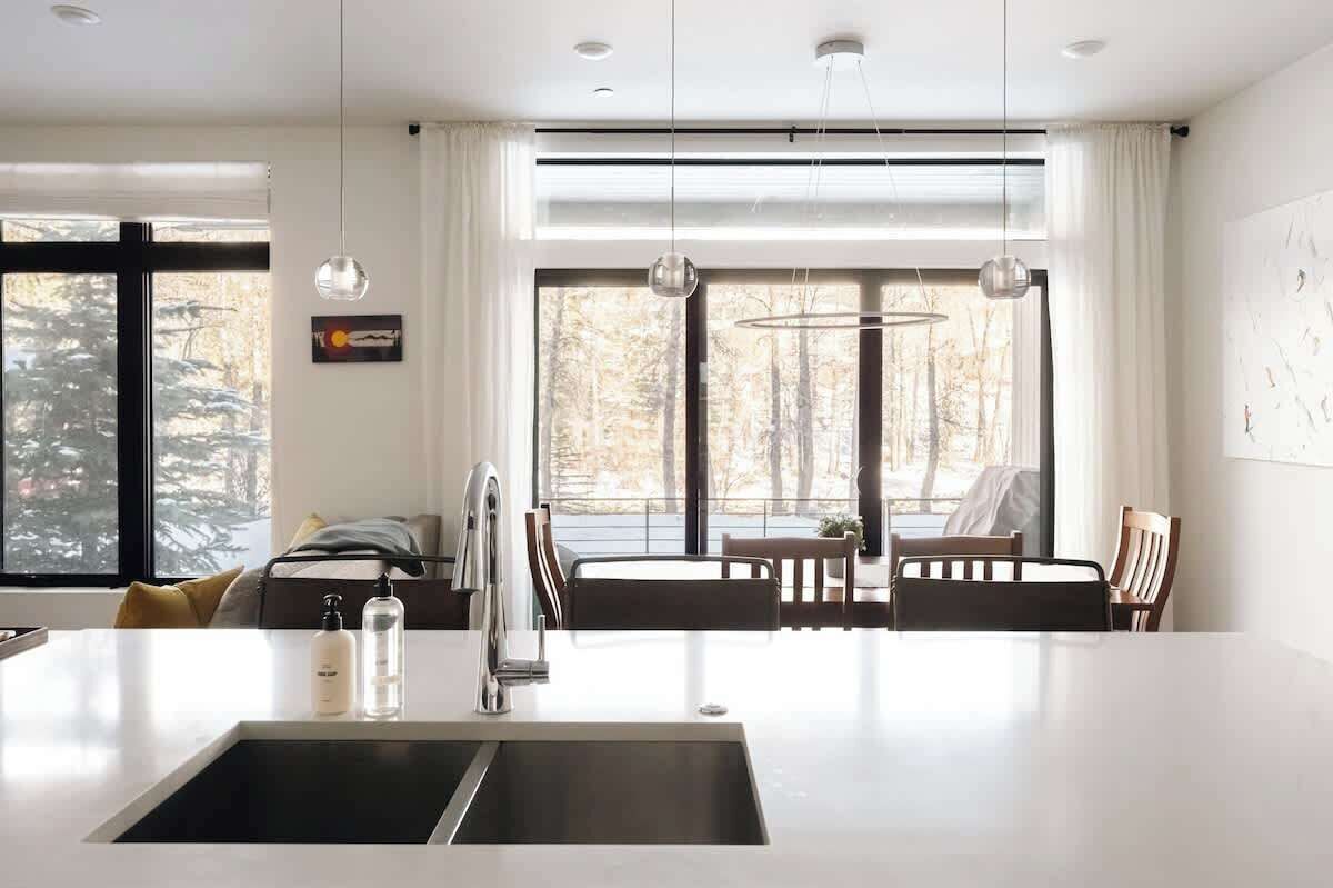 A modern kitchen with a central island, pendant lighting, and large windows with a view of trees.