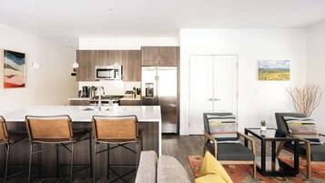 A modern kitchen with a central island, bar stools, and a seating area with a sofa and chairs.