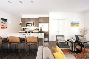 A modern kitchen with a central island, bar stools, and a seating area with a sofa and chairs.
