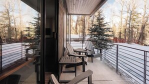 Un balcon avec des sièges d’extérieur, une vue sur une forêt enneigée et une rambarde en métal.