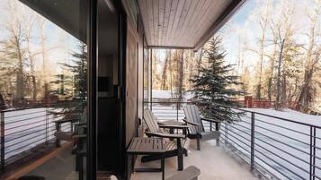 A balcony with outdoor seating, a view of a snowy forest, and a metal railing.
