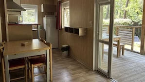 Une cuisine compacte avec des meubles en bois, une table à manger avec des chaises, une cuisinière intégrée et une porte-fenêtre coulissante donnant sur une terrasse extérieure.