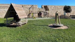 A playground with wooden structures and a stone wall in the background.