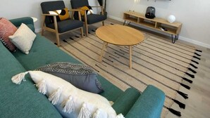 A modern living room with a green sofa, two armchairs, a coffee table, a TV, and a decorative plant.