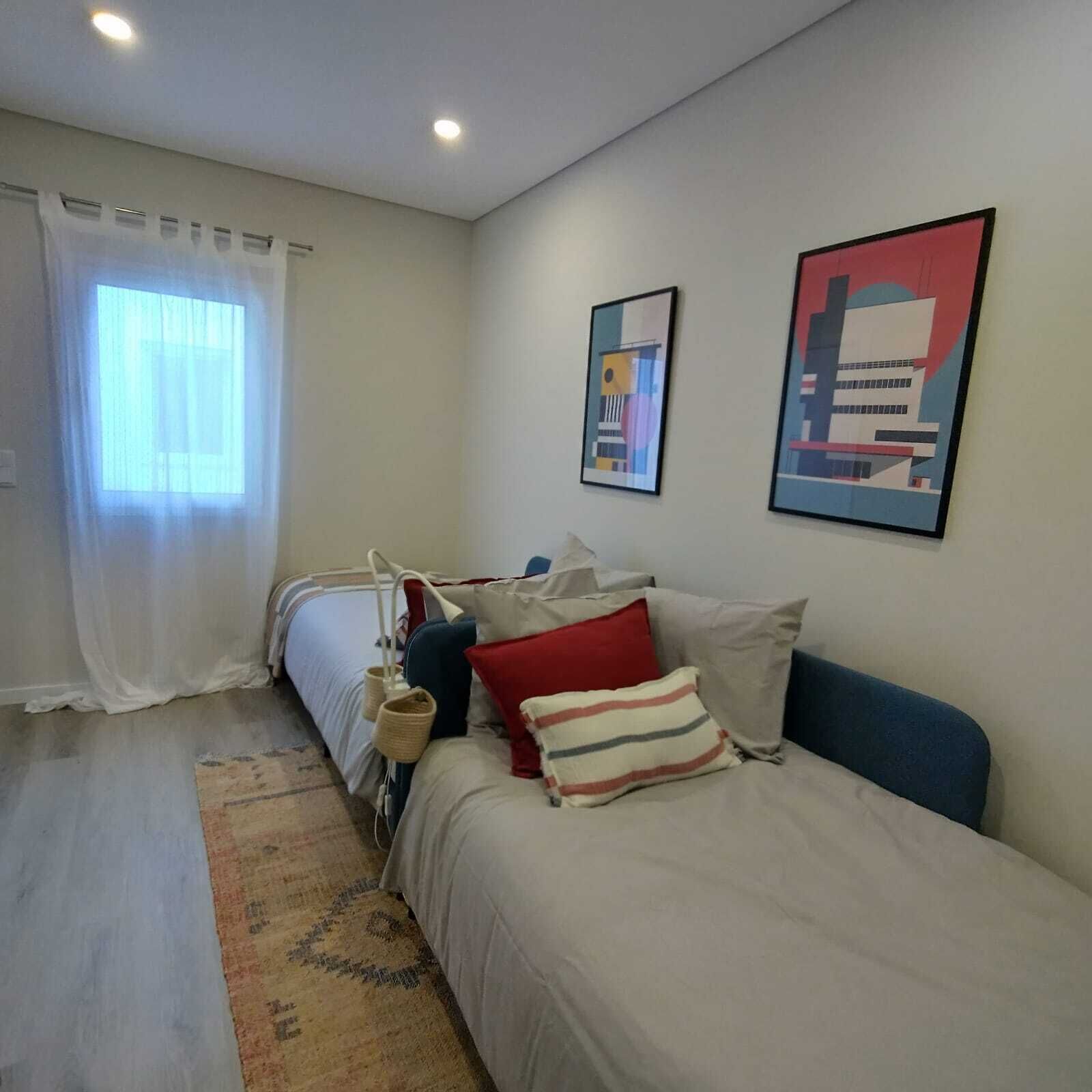Een slaapkamer met een bed, nachtkastje, lamp en twee foto's in lijsten aan de muur.