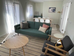 A living room with a green sofa, a round wooden table, and two chairs.