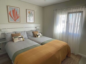 A hotel room with two beds, a nightstand, a lamp, and two framed artworks on the wall.