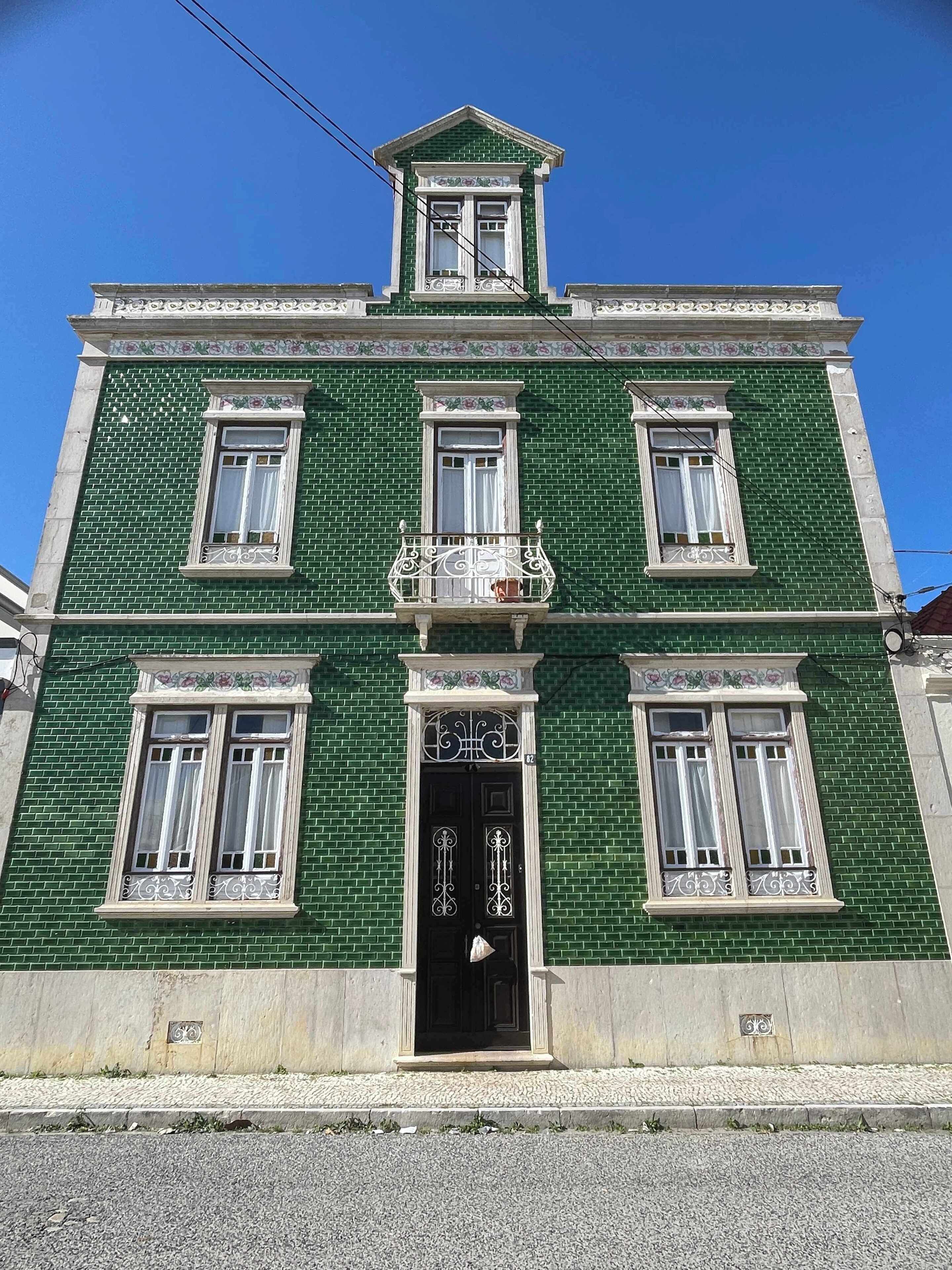 A green building with a central entrance, multiple windows, and a decorative balcony.
