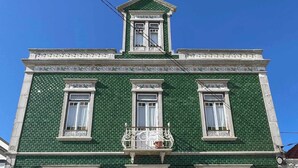 A green building with a central entrance, multiple windows, and a decorative balcony.
