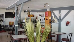 A dining area with tables and chairs, a counter with a cash register, and hanging lights. - ZEcamping 2 étoiles piscine locatif TV clim 23m2 4 pers (Briançonnet)