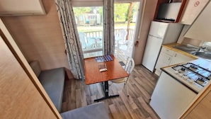 A compact kitchen with a gas stove, a refrigerator, and a dining table with chairs. - ZEcamping 2 étoiles piscine locatif TV clim 23m2 4 pers (Briançonnet)