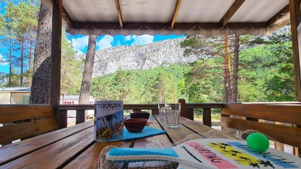 A wooden deck with a table set for dining, overlooking a mountainous landscape. - ZEcamping 2 étoiles piscine locatif TV clim 23m2 4 pers (Briançonnet)