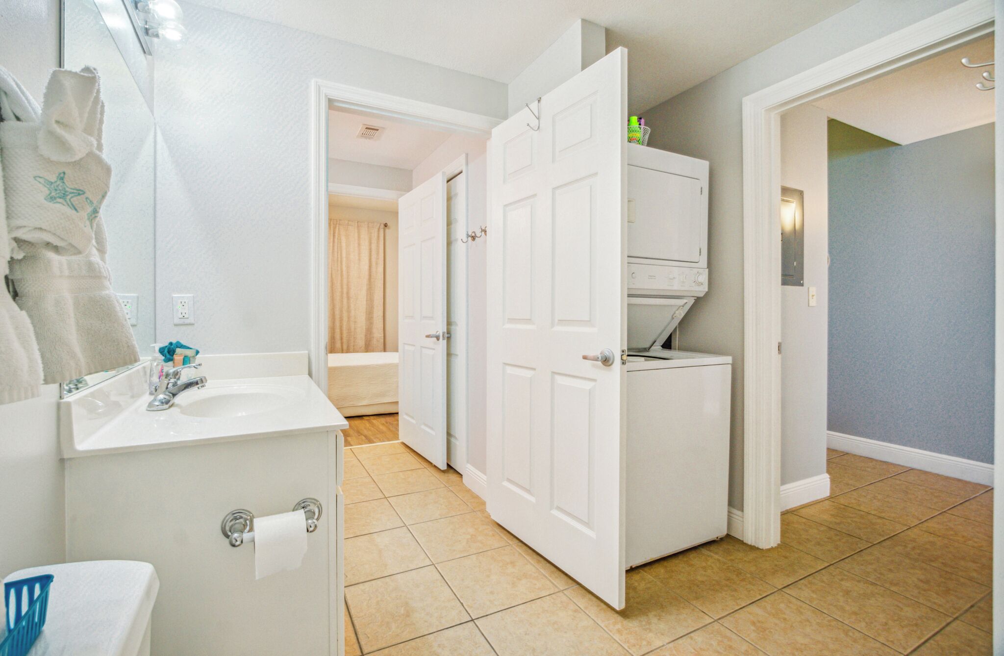 A hotel bathroom with a sink, toilet, and open closet doors leading to a bedroom.