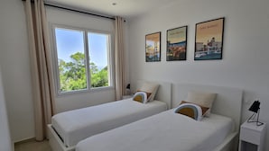 Une chambre d’hôtel avec deux lits, une fenêtre avec des rideaux et trois tableaux encadrés accrochés au mur.