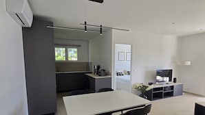 Un espace de vie moderne et compact comprenant un coin cuisine, un espace repas et un petit meuble pour les appareils multimédias.