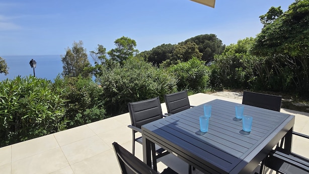 Une terrasse extérieure avec une table et des chaises, un auvent de couleur beige et une vue sur la mer.