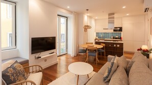 Una sala de estar moderna con un televisor de pantalla plana, un sofá, una mesa de comedor y una zona de cocina con estufa y microondas.