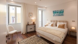 A bedroom with a large bed, a chair, a bedside table, and a window with curtains. - FLH Glória 70 Apartment II (Lisboa ciudad)