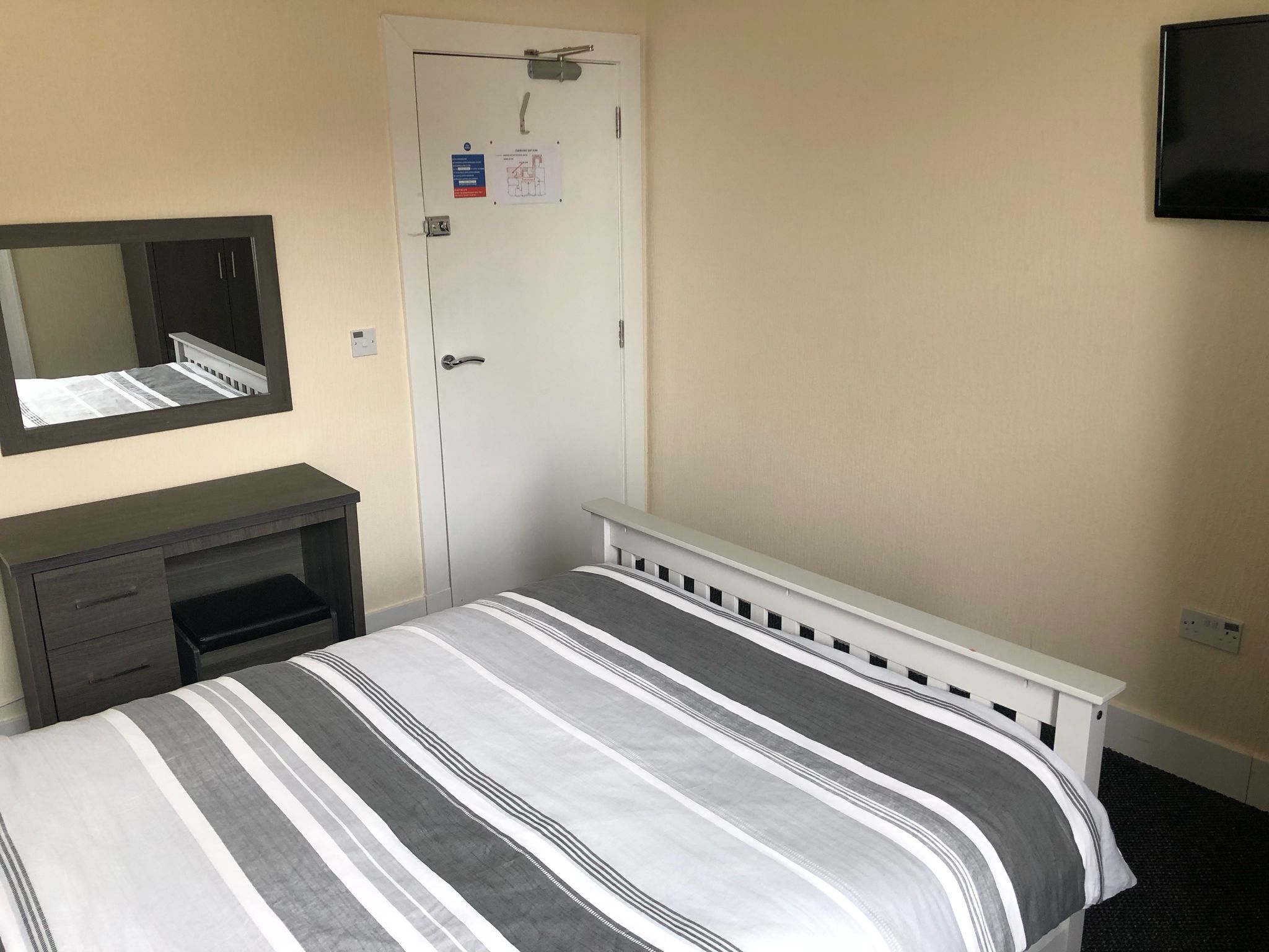 Une chambre d’hôtel avec un lit, une commode, un miroir, une porte et un téléviseur fixé au mur.