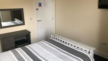 Une chambre d’hôtel avec un lit, une commode, un miroir, une porte et un téléviseur fixé au mur.