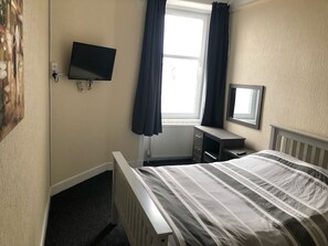 Ein Hotelzimmer mit Bett, Schreibtisch, Fernseher und einem Fenster mit Vorhängen.