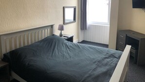 A hotel room with a bed, a bedside table with a lamp, a dresser, a mirror, and a TV on the wall. - Railway Inn (Buckhaven)
