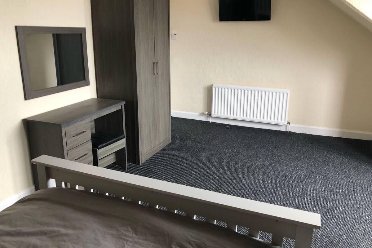 A bedroom with a bed, a wardrobe, a TV, and a radiator.