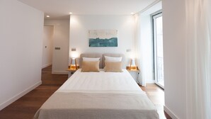A modern bedroom with a large bed, two bedside tables with lamps, a painting on the wall, and a large window with curtains. - FLH Glória 70  Duplex I (Lisbon)