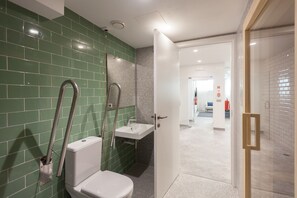 A bathroom with green tiled walls, a white sink, and a toilet.