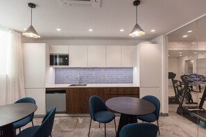 A modern kitchen with white cabinets, a blue backsplash, and a built-in microwave. There is a dining area with a round table and blue chairs.