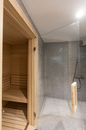 Un sauna en bois avec une porte en verre, un espace douche avec un mur en marbre et un petit banc en bois.