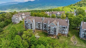 Un complejo residencial con varias edificaciones, rodeado de exuberante vegetación y montañas al fondo.