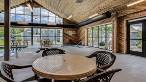 Un espacio interior amplio con una mesa grande y sillas, un jacuzzi y ventanas grandes que ofrecen vistas al exterior.