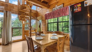 A wooden cabin interior with a dining table set for four, a spiral staircase, and a large window overlooking greenery. - Sweet Bearoline-Great Views, Game Roon, Close to Dollywood (Sevierville)
