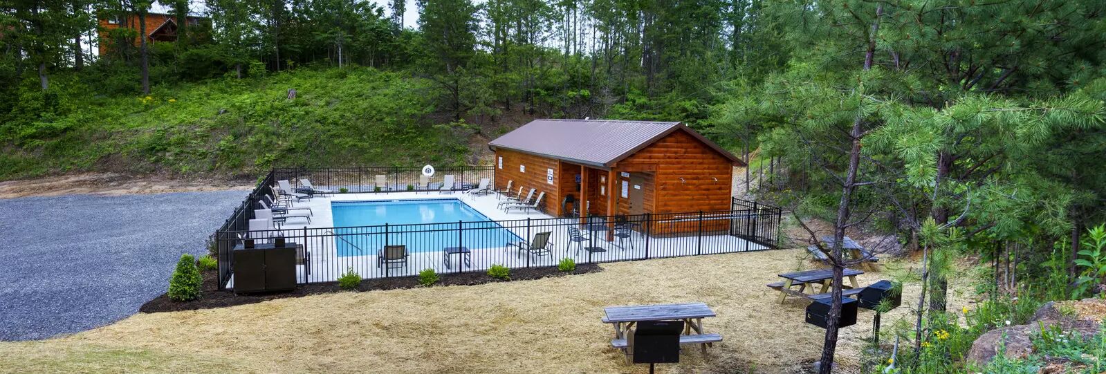 A cabin with a swimming pool, surrounded by a fence and picnic tables.