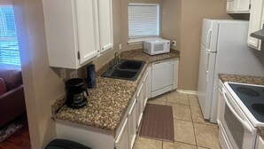 A compact kitchen with white cabinets, a microwave, a stove, and a sink.