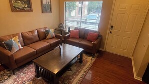 A living room with a sectional sofa, a coffee table, a ceiling fan, and a window with blinds.