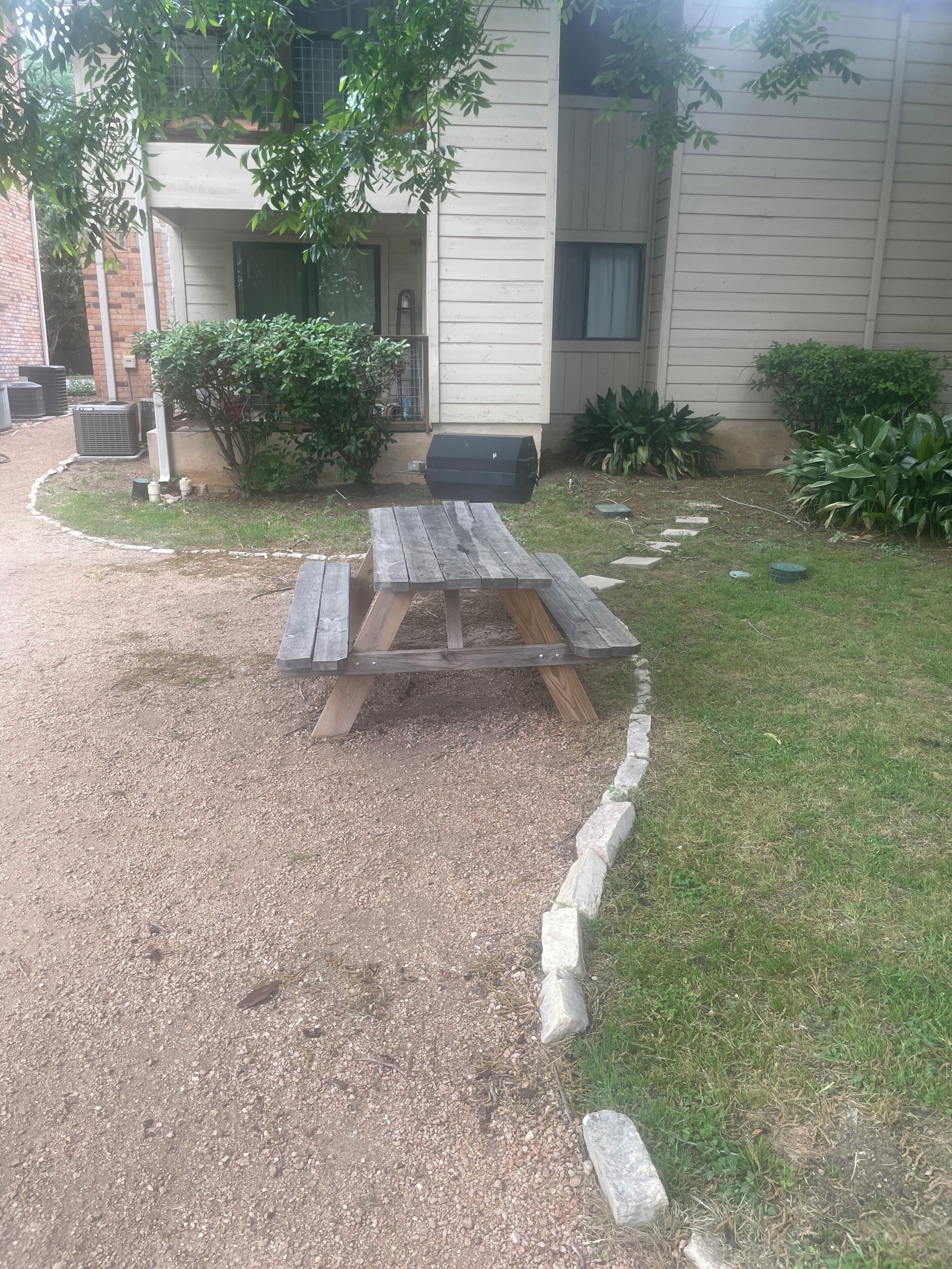 A gravel patio with a wooden picnic table, surrounded by a low stone border.