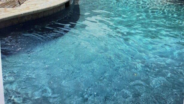 A swimming pool with a stone border, lounge chairs, and a building in the background.